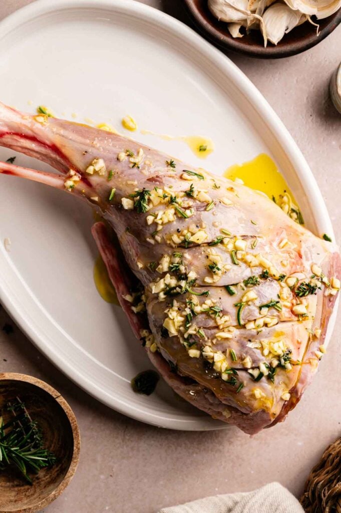 Herb-crusted leg of lamb ready for roasting, with fresh rosemary and garlic nearby.
