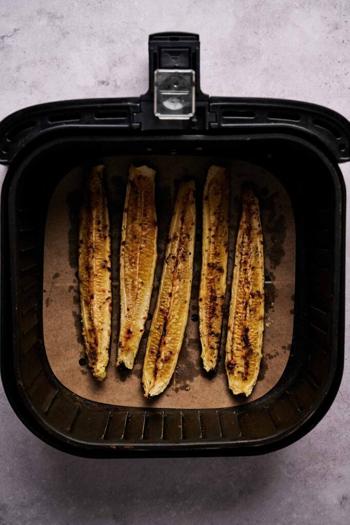Six Air Fryer Baked Zucchini halves rest on parchment paper inside an air fryer basket, photographed from above.