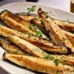 Air Fryer Baked Zucchini halves are garnished with chopped herbs and served on a white dish, creating a delicious and healthy presentation.