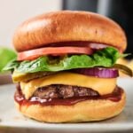 An Air Fryer Cheeseburger with lettuce, tomato, pickles, red onion, and melted cheese on a bun, served on a plate.