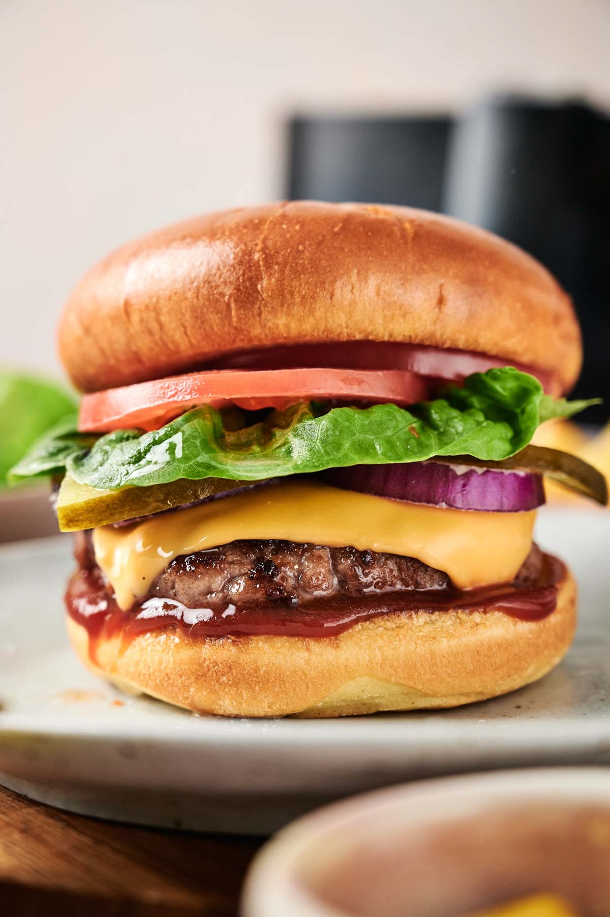 An Air Fryer Cheeseburger with lettuce, tomato, pickles, red onion, and melted cheese on a bun, served on a plate.