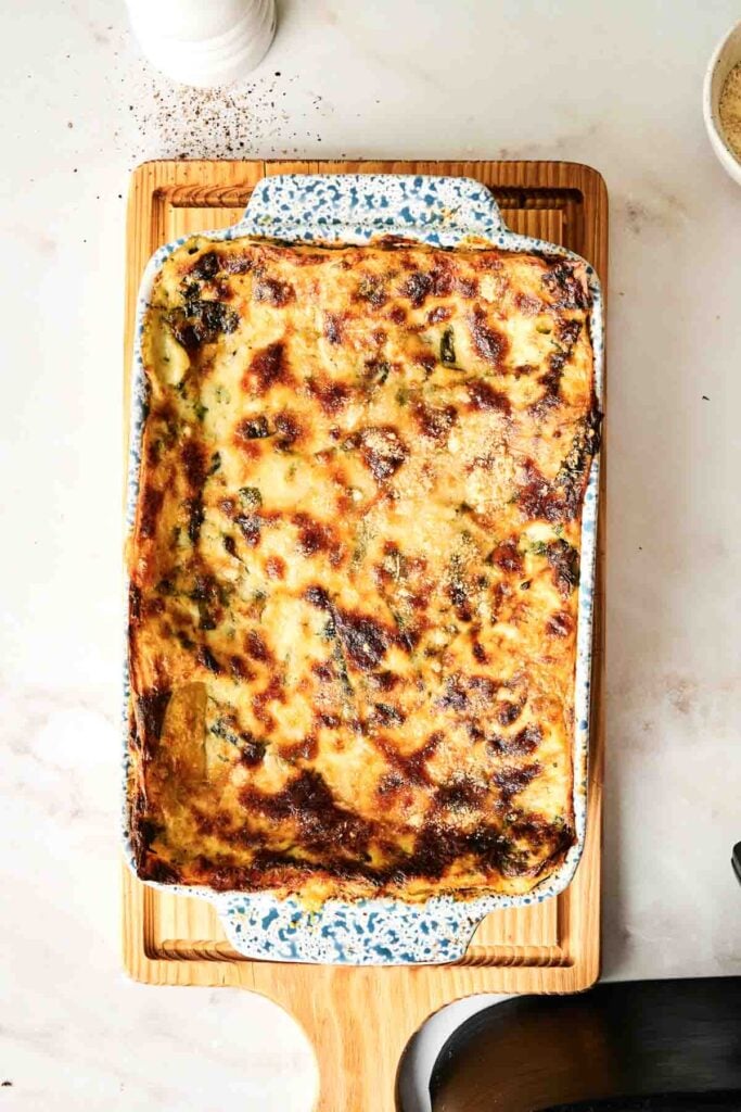A baked Air fryer Chicken Alfredo Lasagna with a golden-brown, bubbly cheese topping sits in a rectangular ceramic dish on a wooden cutting board.