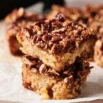 Two Air Fryer Pecan Pie Bars stacked on top of each other, featuring a crumbly base and nut topping, rest on a piece of parchment paper.