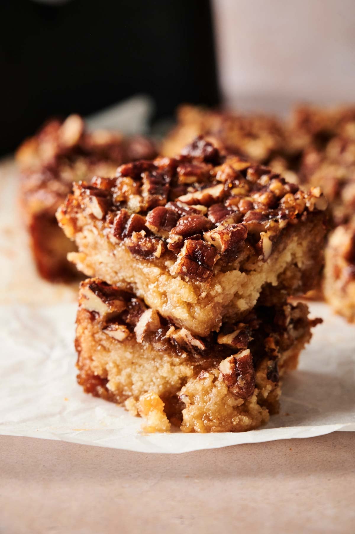 Two Air Fryer Pecan Pie Bars stacked on top of each other, featuring a crumbly base and nut topping, rest on a piece of parchment paper.