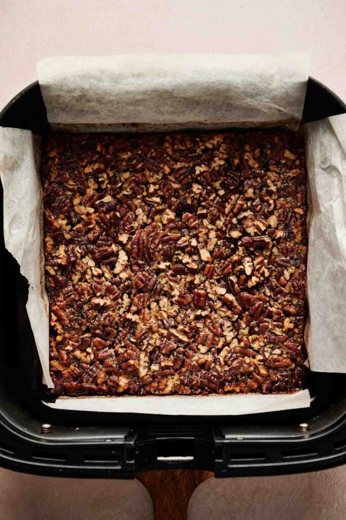 Air Fryer Pecan Pie Bars baked in a square pan lined with parchment paper, viewed from above.