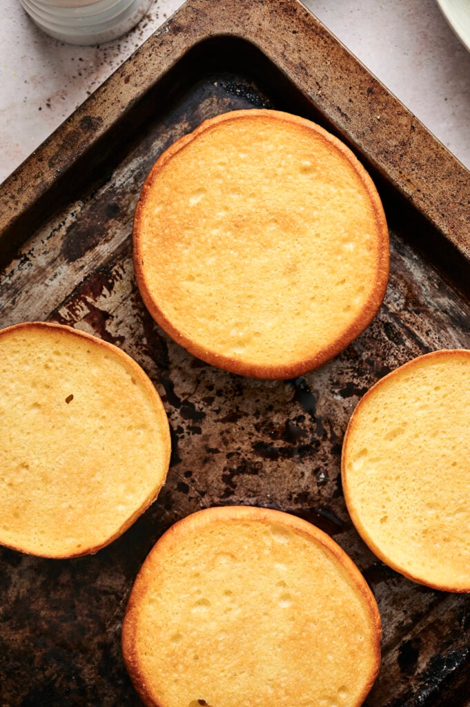 Four golden brown pancake-like rounds on a baking sheet, viewed from above&mdash;perfect as buns for your next Air Fryer Cheeseburger.