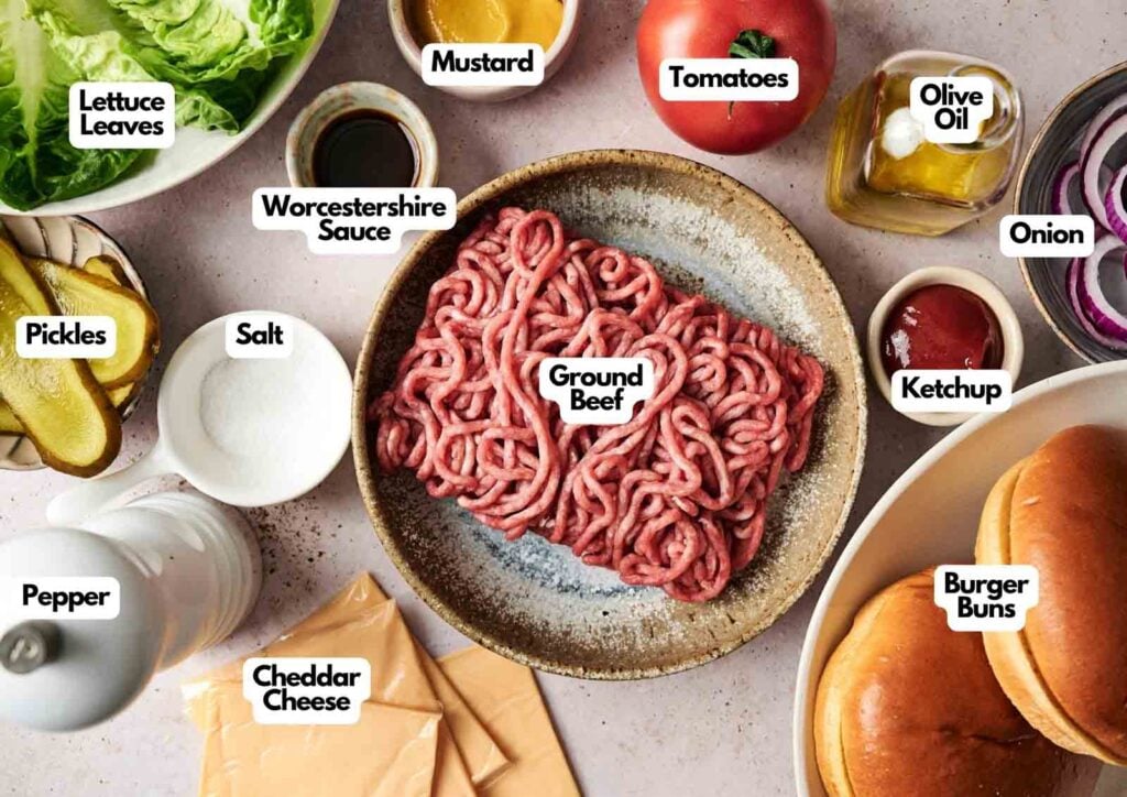 A plate of raw ground beef is surrounded by labeled burger ingredients, perfect for crafting an Air Fryer Cheeseburger&mdash;lettuce, tomato, onion, pickles, cheddar cheese, buns, ketchup, mustard, olive oil, Worcestershire sauce, salt, and pepper.