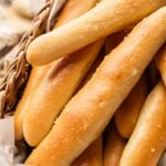 A basket filled with several golden-brown Copycat Olive Garden Breadsticks, each topped with a light sprinkle of salt.