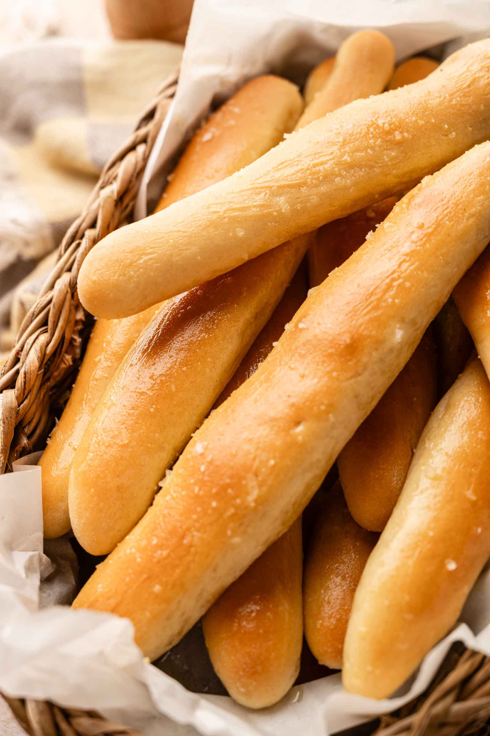 A basket filled with several golden-brown Copycat Olive Garden Breadsticks, each topped with a light sprinkle of salt.