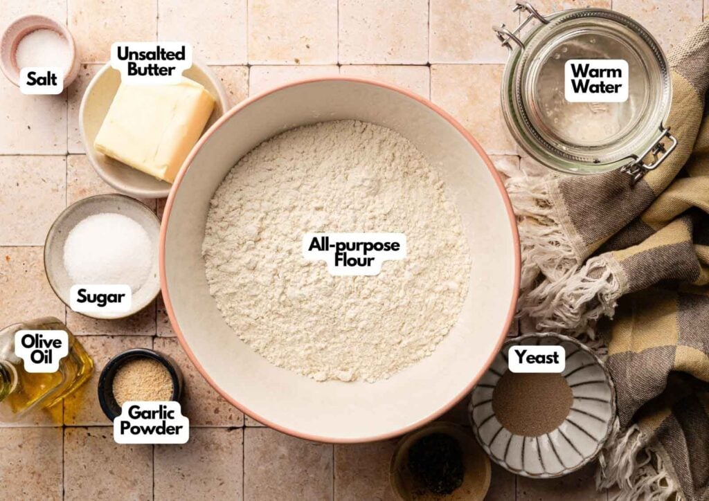 Ingredients for Copycat Olive Garden Breadsticks dough displayed in bowls: all-purpose flour, unsalted butter, warm water, salt, sugar, olive oil, garlic powder, and yeast.