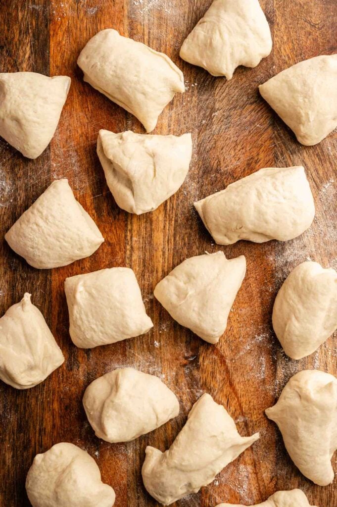 Several pieces of raw dough for copycat Olive Garden breadsticks are spaced out on a wooden surface dusted with flour.