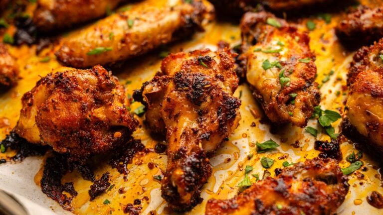 Baked chicken wings with a crispy, seasoned coating on a baking sheet, garnished with chopped herbs.