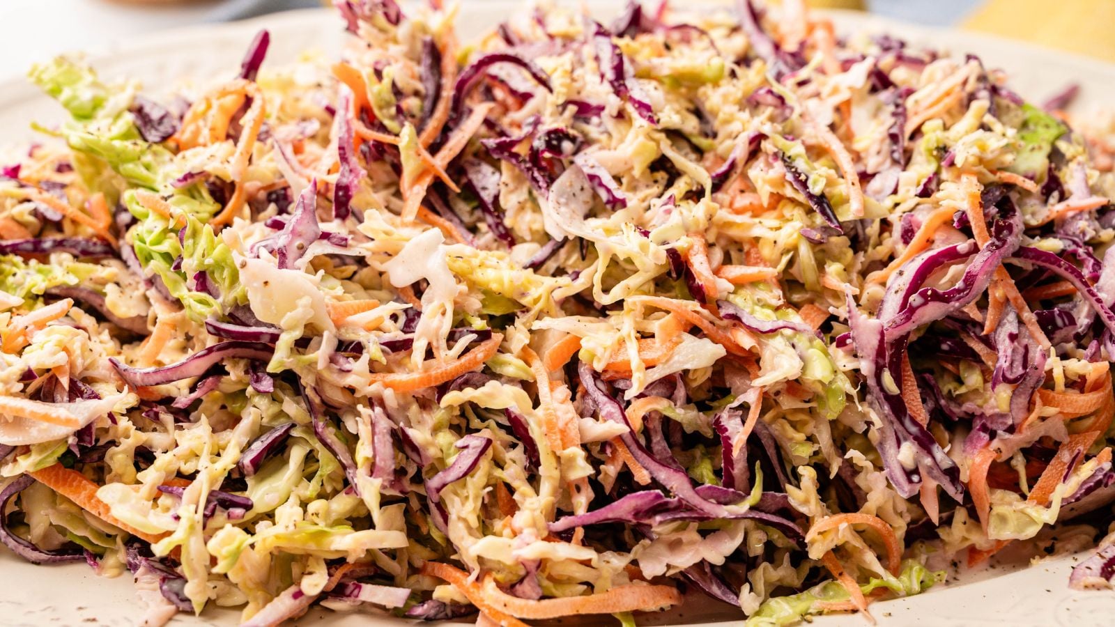 A close-up of coleslaw made with shredded green and purple cabbage, carrots, and creamy dressing on a white plate.