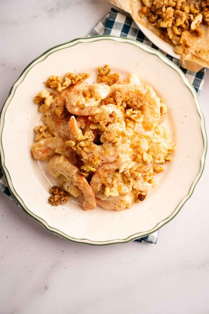 A plate of creamy Panda Express Honey Walnut Shrimp topped with chopped walnuts, served on a white plate with a green rim on a checkered cloth.