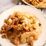 A plate of creamy Panda Express Honey Walnut Shrimp topped with caramelized walnuts, with extra walnuts on parchment paper in the background.