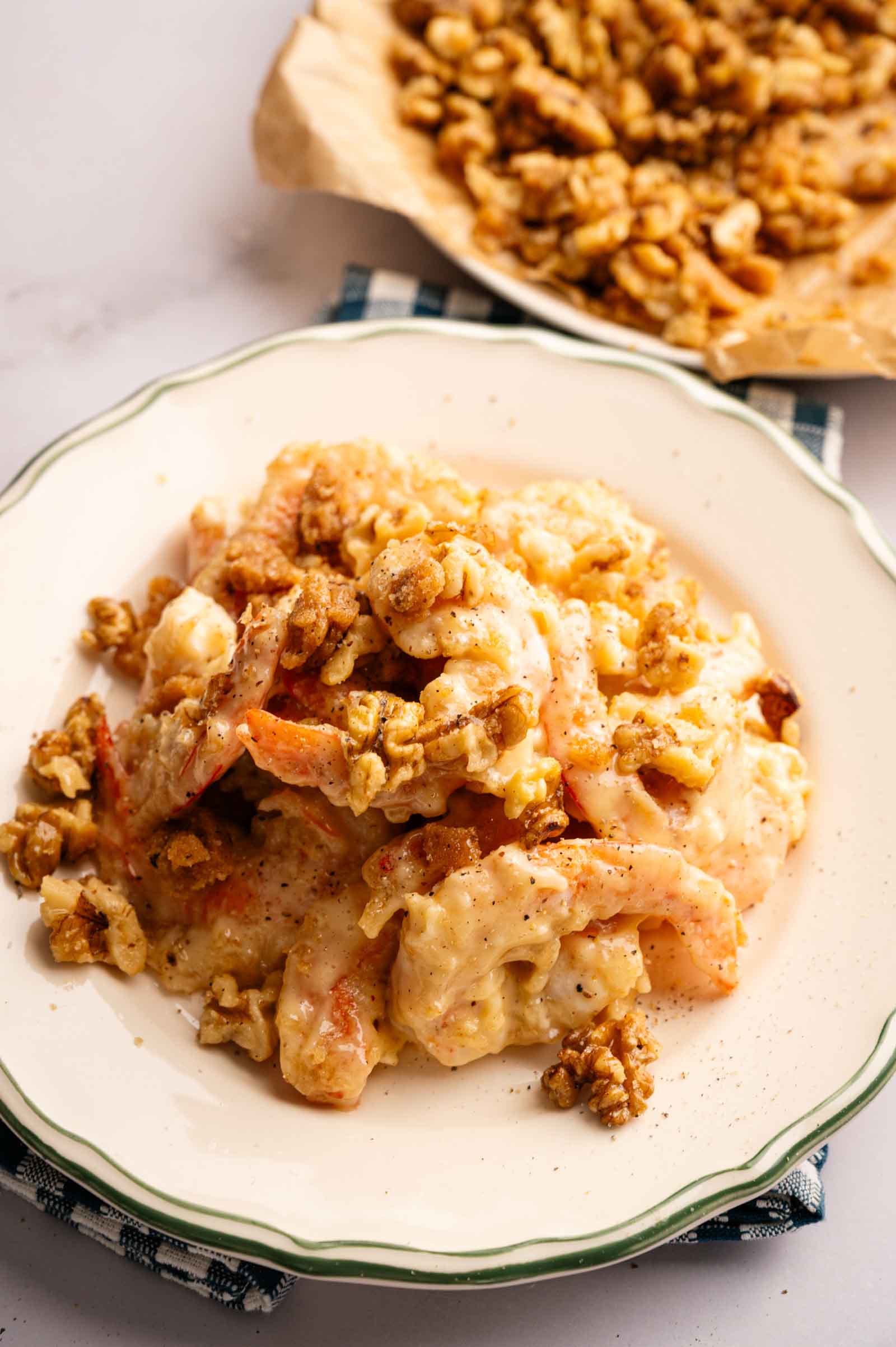 A plate of creamy Panda Express Honey Walnut Shrimp topped with caramelized walnuts, with extra walnuts on parchment paper in the background.