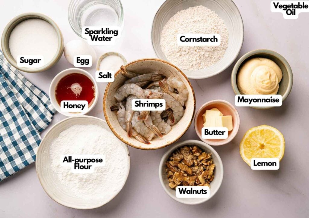Top-down view of bowls containing labeled ingredients for a Panda Express Honey Walnut Shrimp recipe, including shrimp, flour, sugar, egg, sparkling water, honey, salt, cornstarch, mayonnaise, butter, lemon, walnuts, and vegetable oil.