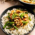 A bowl of white rice topped with stir-fried chicken, green beans, and cashews, inspired by Panda Express String Bean Chicken Breast, and garnished with black sesame seeds.