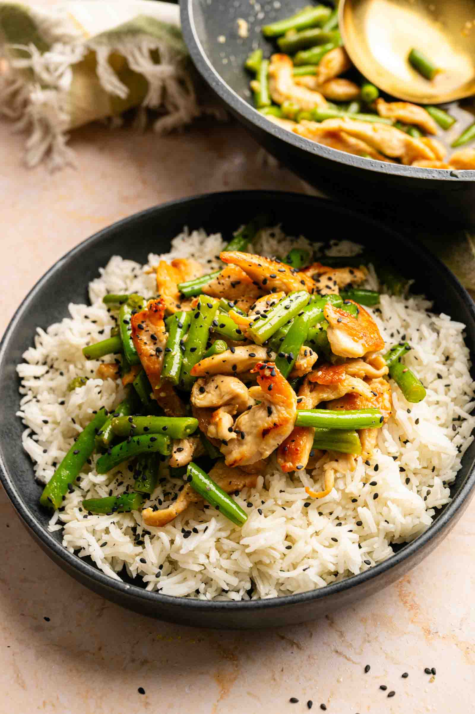 A bowl of white rice topped with stir-fried chicken, green beans, and cashews, inspired by Panda Express String Bean Chicken Breast, and garnished with black sesame seeds.