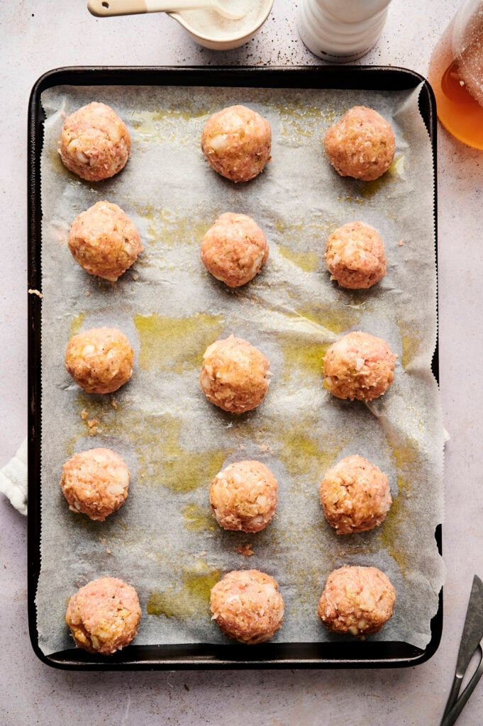 A baking tray lined with parchment paper holds fifteen evenly spaced raw Air Fryer Turkey Meatballs, ready for cooking.