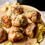Five Air Fryer Turkey Meatballs covered in creamy brown gravy are served over mashed potatoes and garnished with chopped parsley on a white plate.