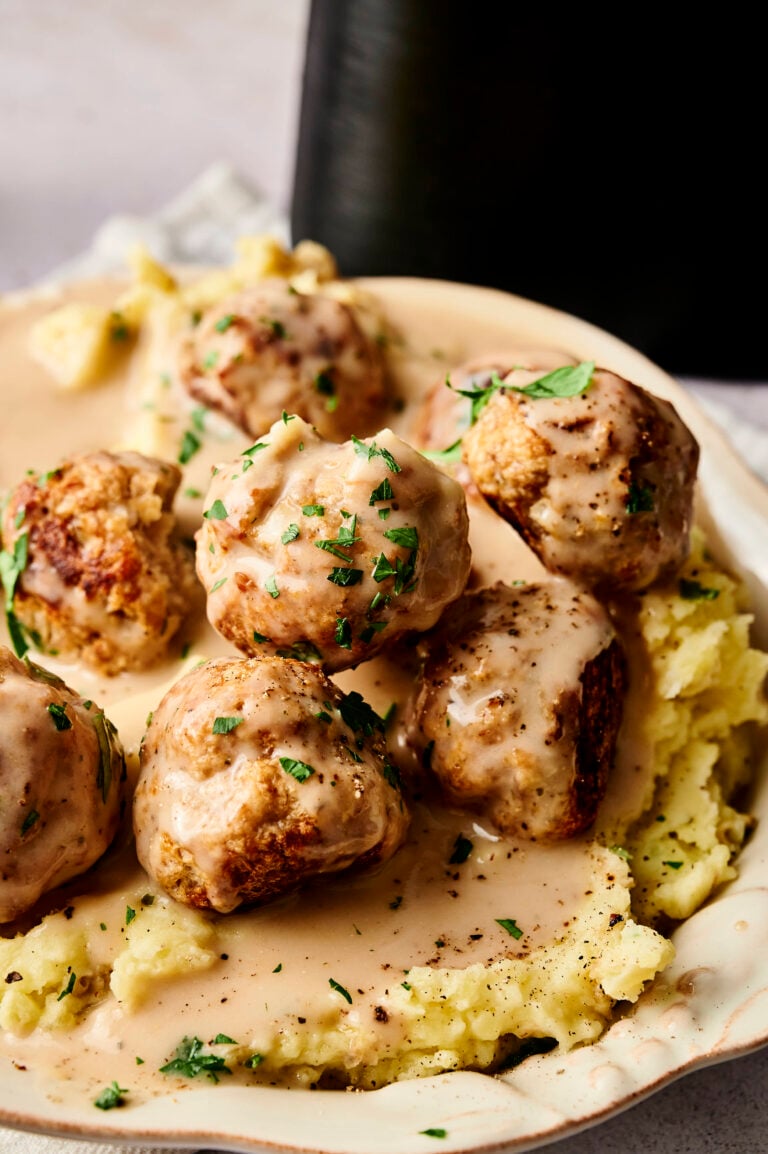 Five Air Fryer Turkey Meatballs covered in creamy brown gravy are served over mashed potatoes and garnished with chopped parsley on a white plate.