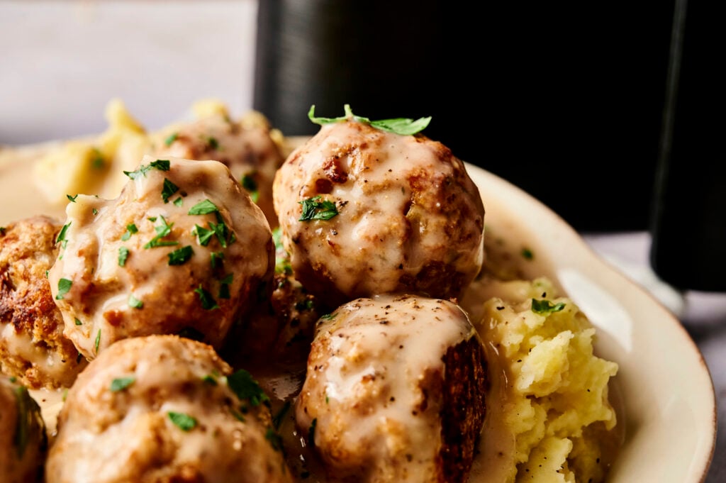 A plate of Air Fryer Turkey Meatballs topped with creamy brown gravy and chopped herbs, served alongside mashed potatoes.