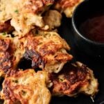 A plate of golden-brown Air Fryer Chicken Fritters is served next to a small black bowl of dipping sauce.