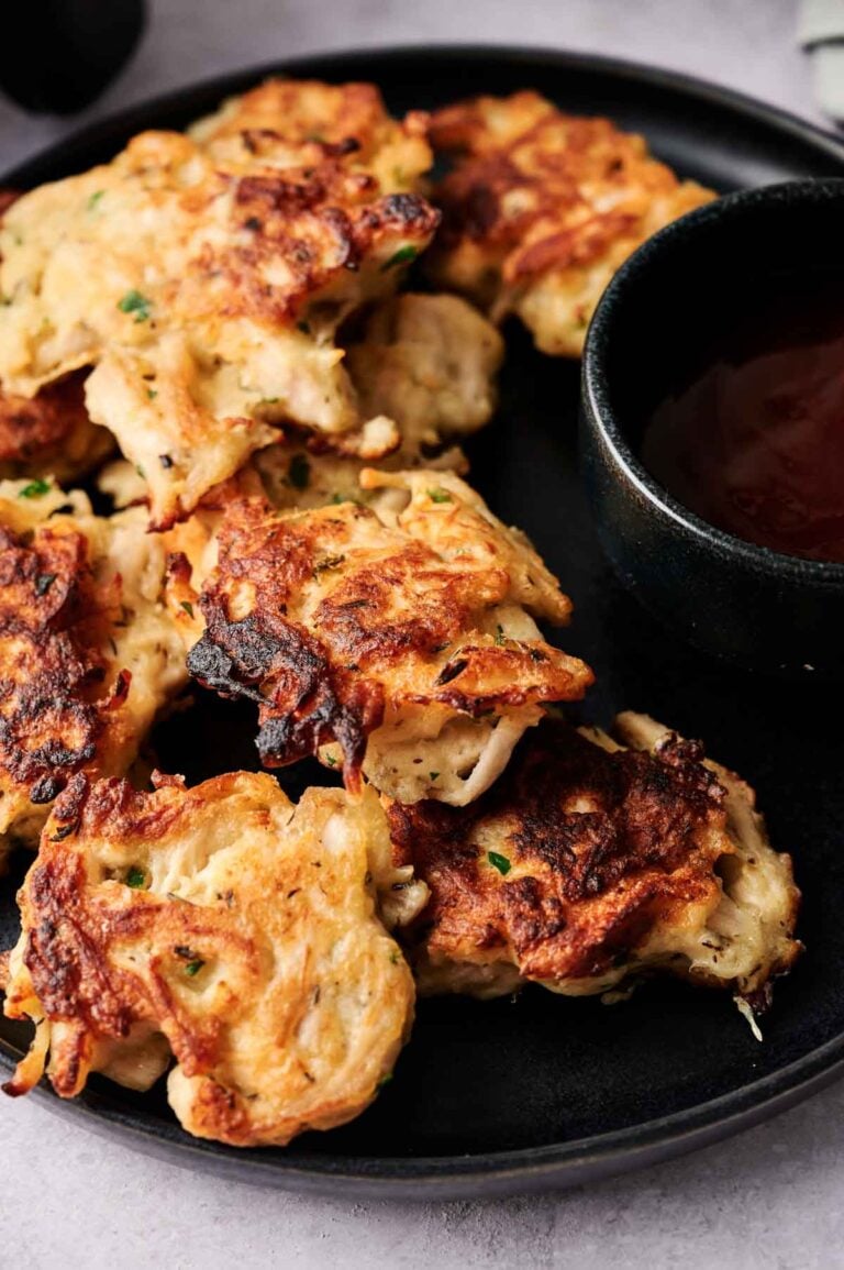 A plate of golden-brown Air Fryer Chicken Fritters is served next to a small black bowl of dipping sauce.