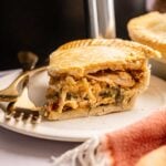 A slice of Air Fryer Marry Me Chicken Pot Pie filled with creamy chicken and vegetables sits on a white plate with a fork and knife beside it.