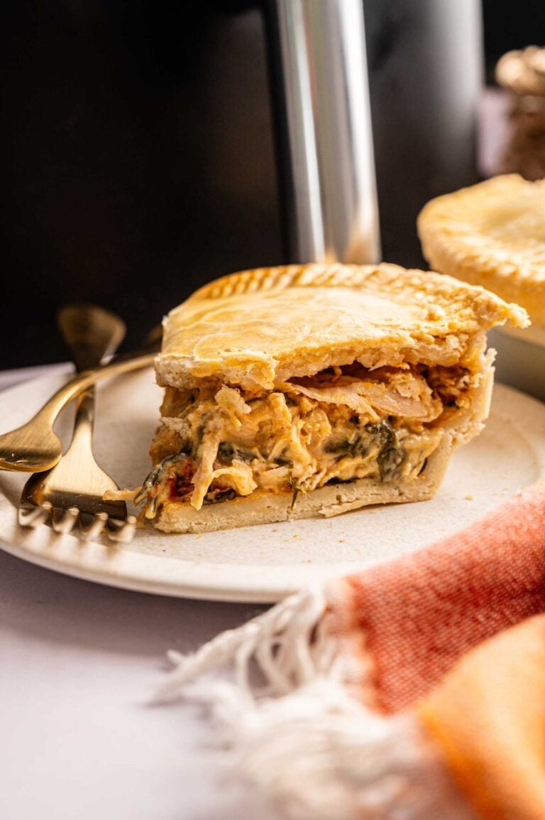 A slice of Air Fryer Marry Me Chicken Pot Pie filled with creamy chicken and vegetables sits on a white plate with a fork and knife beside it.