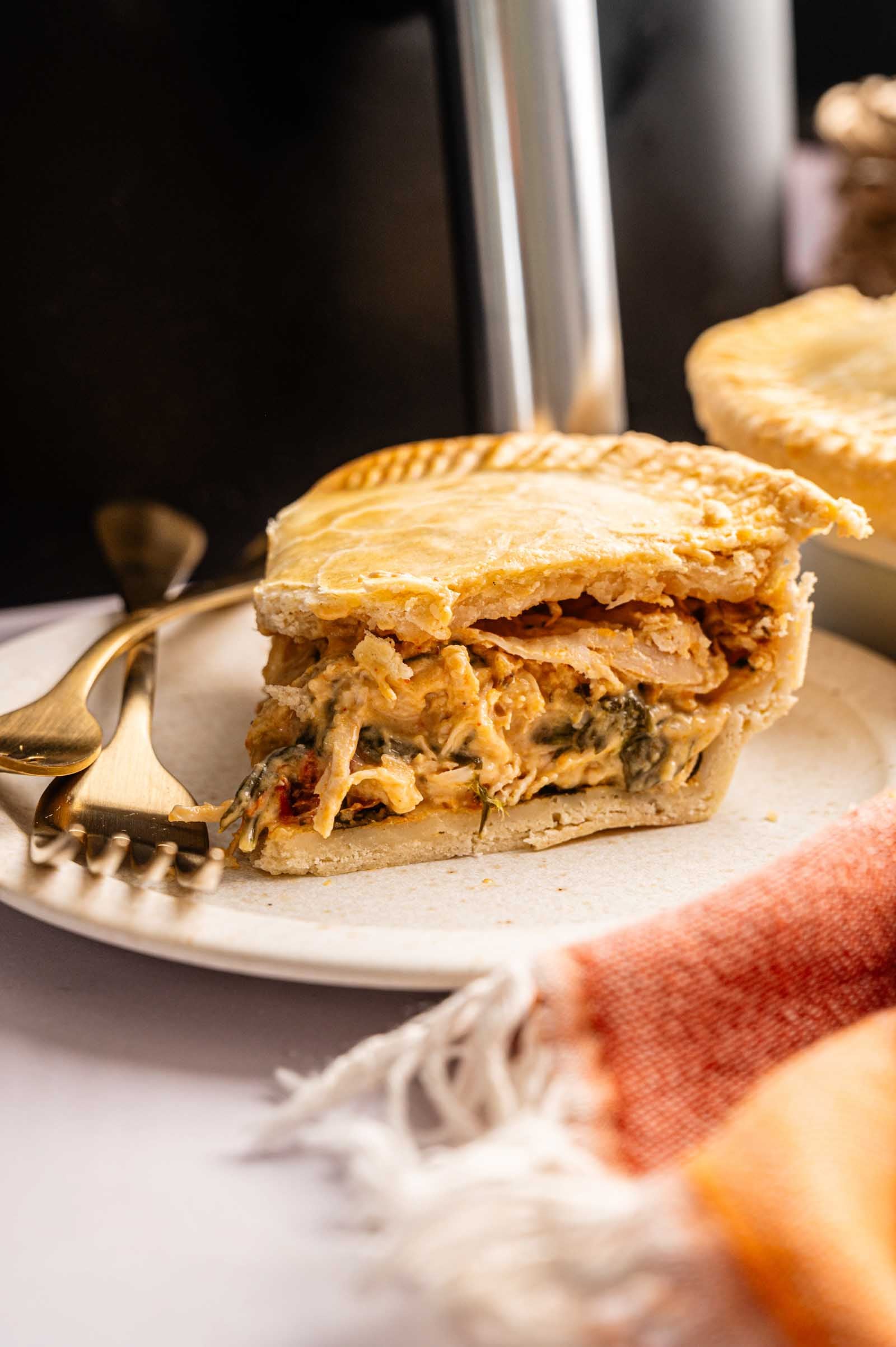 A slice of Air Fryer Marry Me Chicken Pot Pie filled with creamy chicken and vegetables sits on a white plate with a fork and knife beside it.