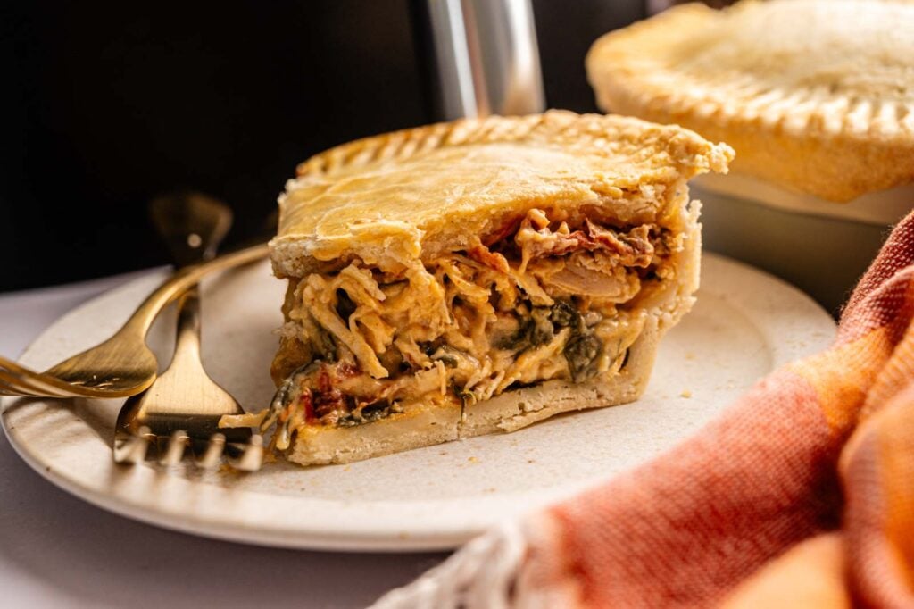 A slice of savory Air Fryer Marry Me Chicken Pot Pie with a golden crust and creamy filling of shredded chicken and vegetables, served on a plate with a fork and knife.