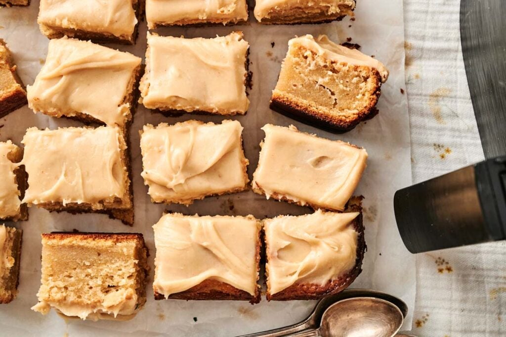 Several slices of air fryer peanut butter cake are arranged on parchment paper beside two metal spoons.