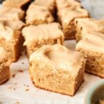 Several slices of air fryer peanut butter cake are arranged on parchment paper beside two metal spoons.