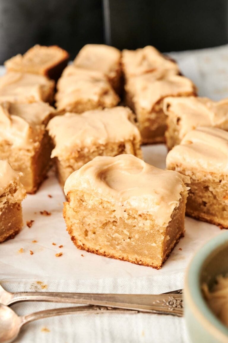 Several slices of air fryer peanut butter cake are arranged on parchment paper beside two metal spoons.