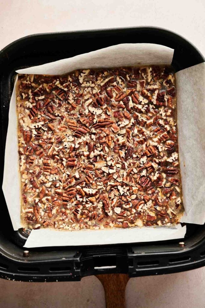 Pecan pie bars topped with chopped pecans in a parchment-lined air fryer basket