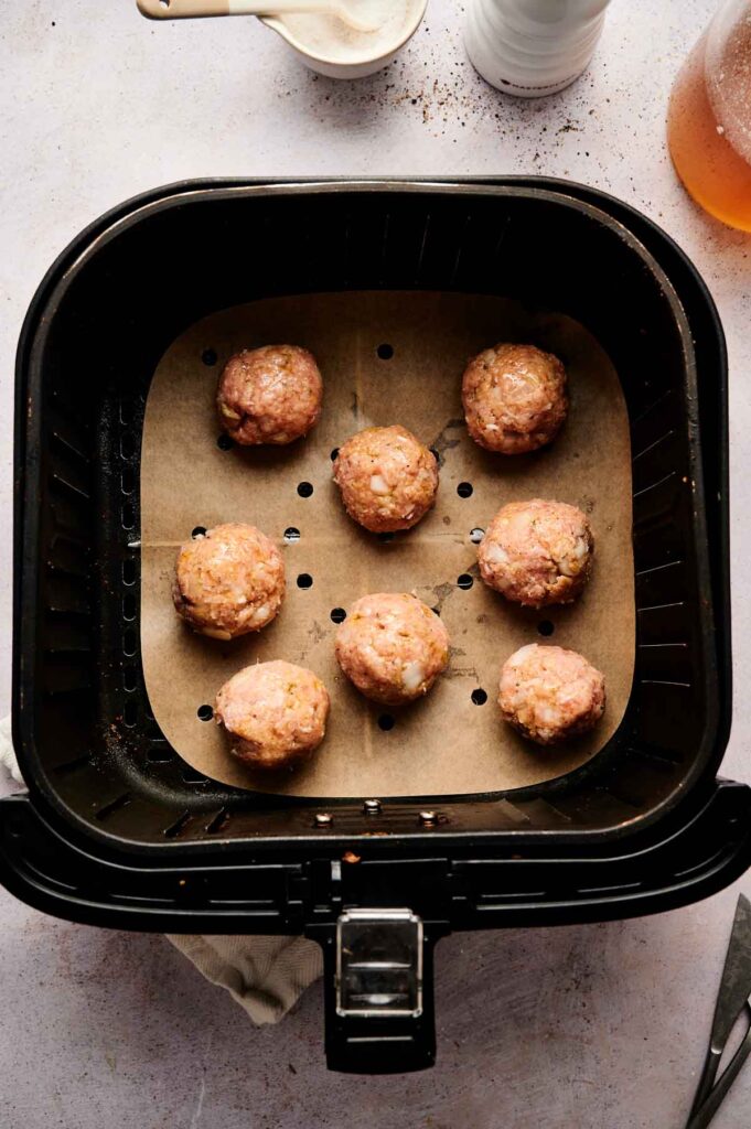 Eight raw Air Fryer Turkey Meatballs are arranged on parchment paper inside an air fryer basket, ready to be cooked.