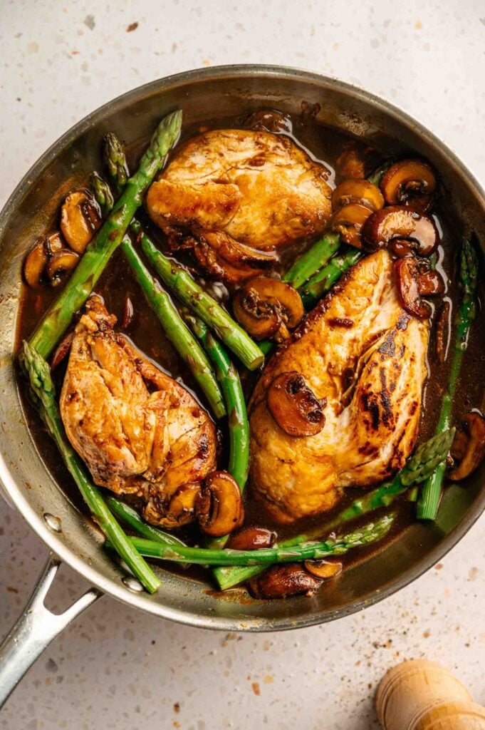 Seared chicken breasts simmering with asparagus and mushrooms in a rich wine sauce.