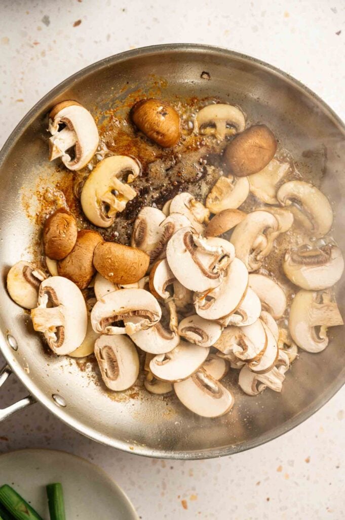 Sliced mushrooms browning in butter in a stainless steel skillet.