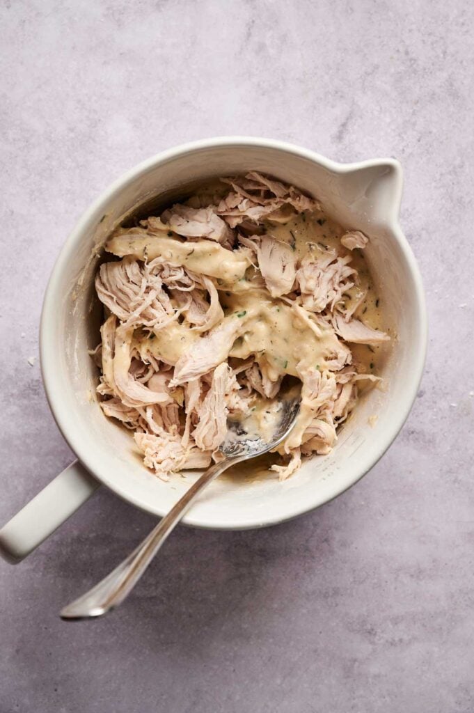 Shredded chicken mixed with a creamy sauce in a white bowl, perfect as a filling for Air Fryer Chicken Fritters, with a metal spoon resting inside.