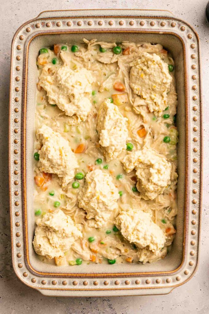 Rectangular baking dish filled with a creamy mixture of chicken, peas, and carrots, topped with large dollops of Cheddar Bay biscuit dough—this Chicken Pot Pie with Cheddar Bay Biscuits is ready to be baked.