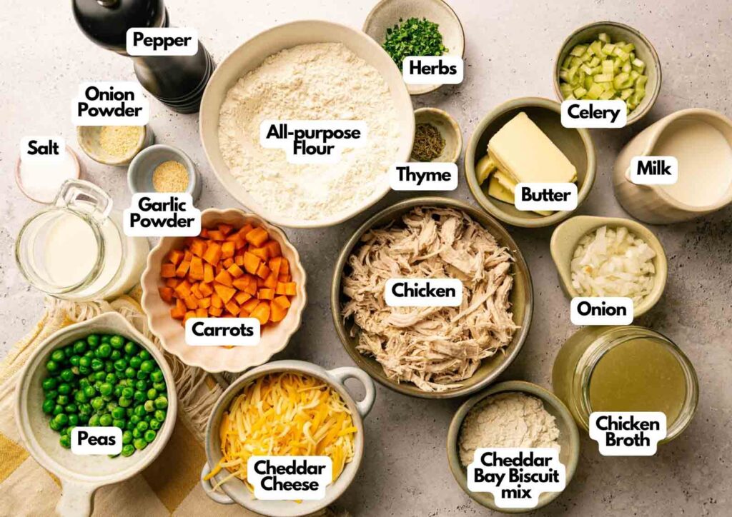Ingredients for Chicken Pot Pie with Cheddar Bay Biscuits are arranged in bowls, including chicken, flour, peas, carrots, cheese, milk, broth, onion, celery, butter, herbs, and seasonings.