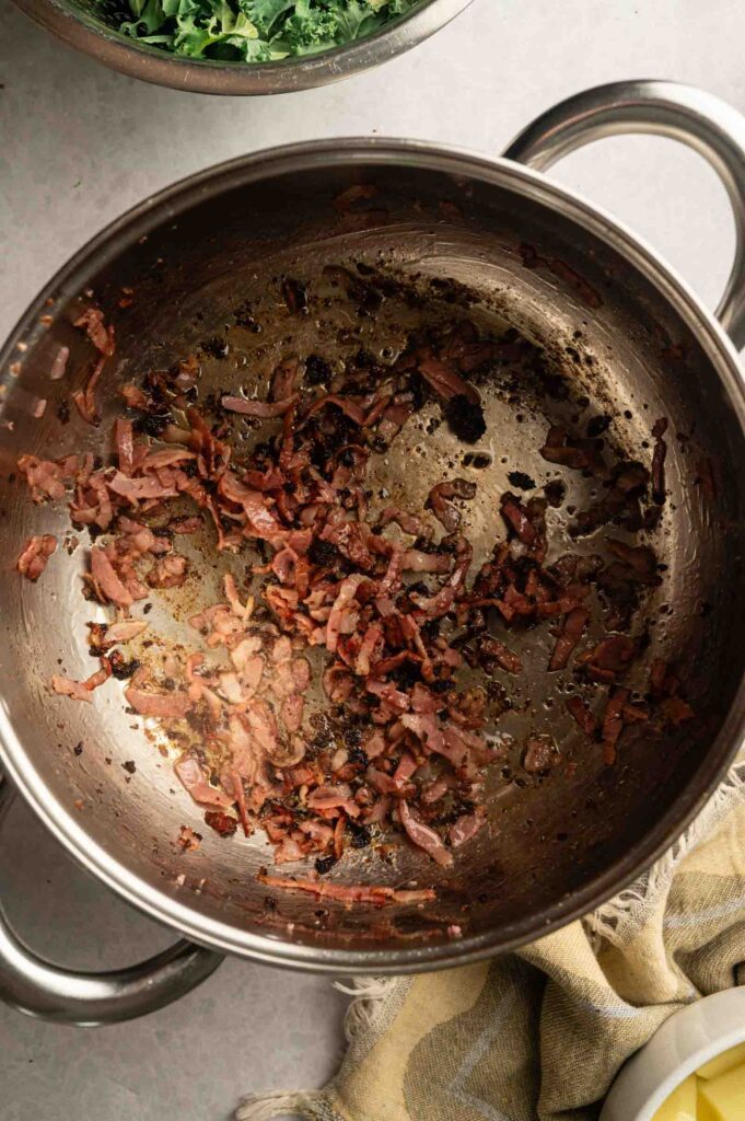 Sautéed onions and chopped bacon pieces in a stainless steel pot, viewed from above—perfect as the flavorful base for a copycat Olive Garden Zuppa Toscana.