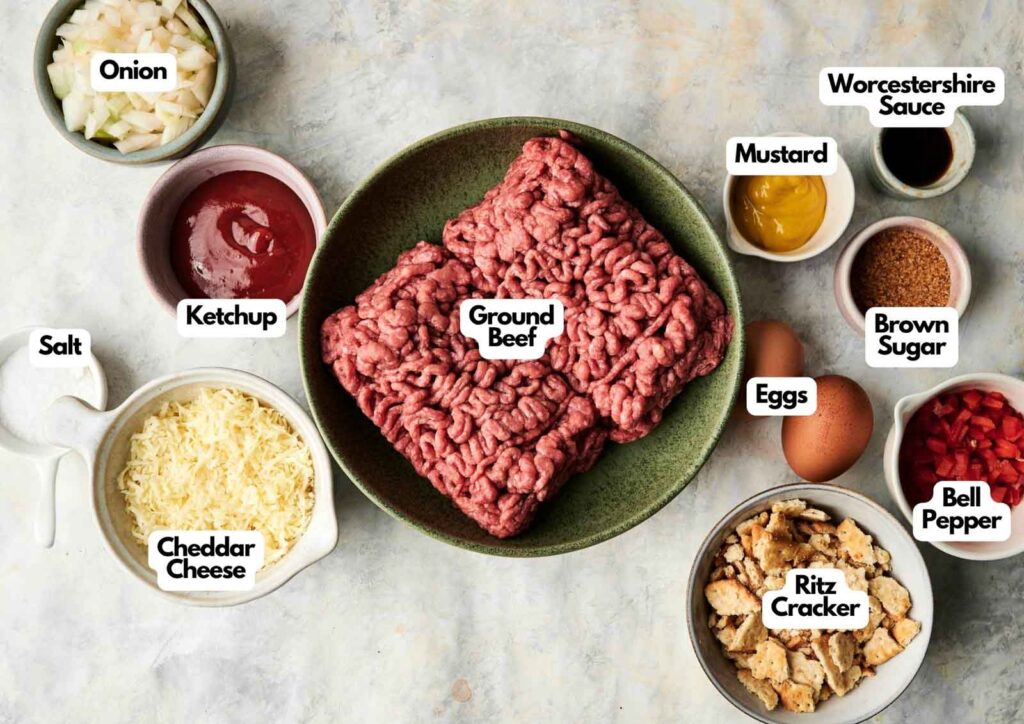 Overhead view of labeled ingredients for Air Fryer Cracker Barrel Meatloaf, including ground beef, eggs, bell pepper, onion, ketchup, mustard, Worcestershire sauce, salt, cheddar cheese, brown sugar, and Ritz crackers.