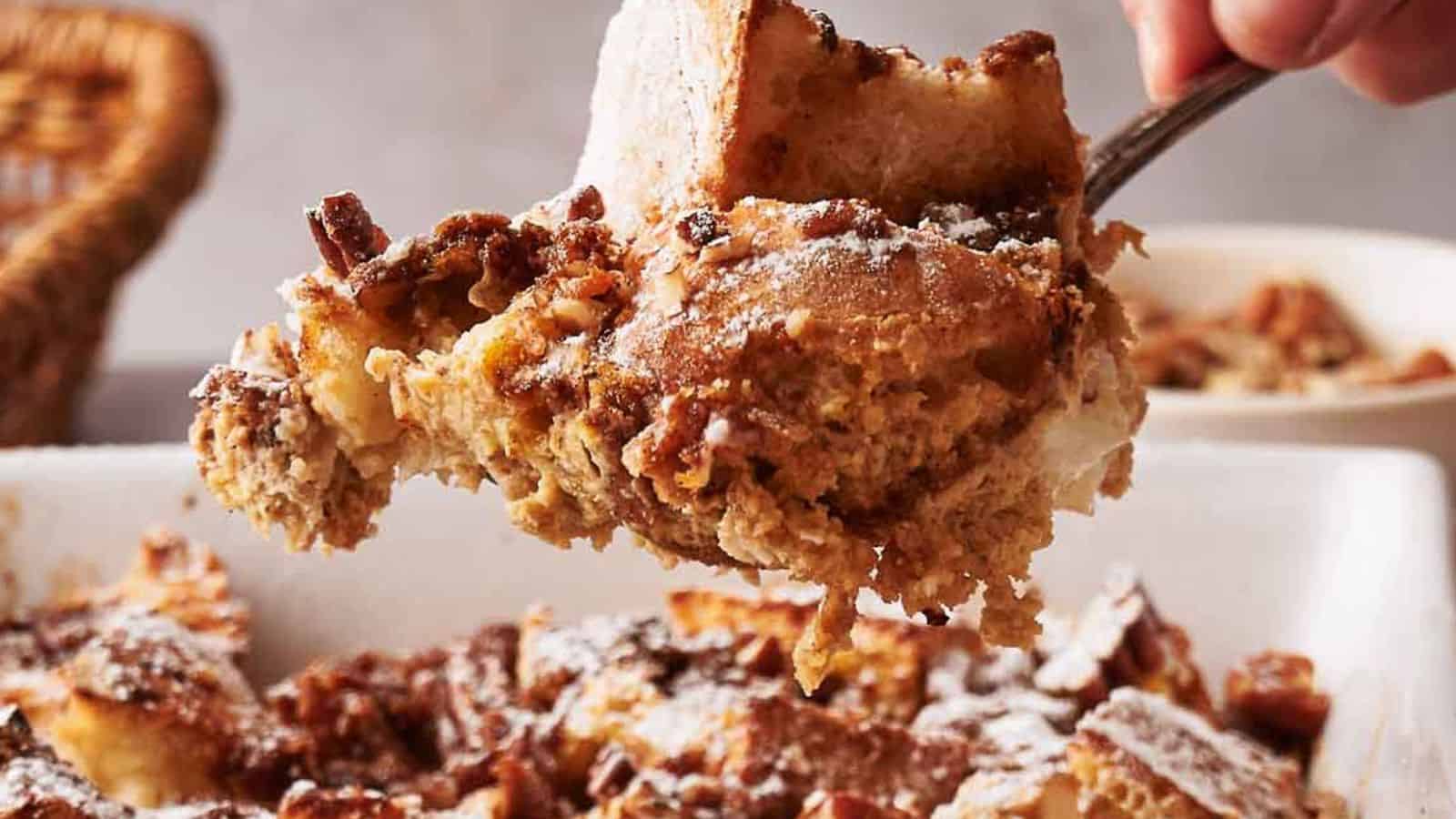 A close-up of a serving of bread pudding being lifted from a baking dish, dusted with powdered sugar.