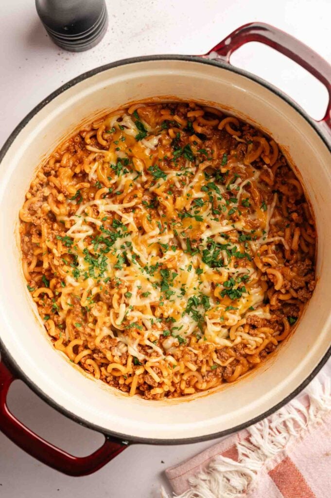 A pot of cooked macaroni with ground meat, tomato sauce, melted cheese, and chopped parsley, viewed from above—just like a homemade Hamburger Helper Cheeseburger Macaroni.