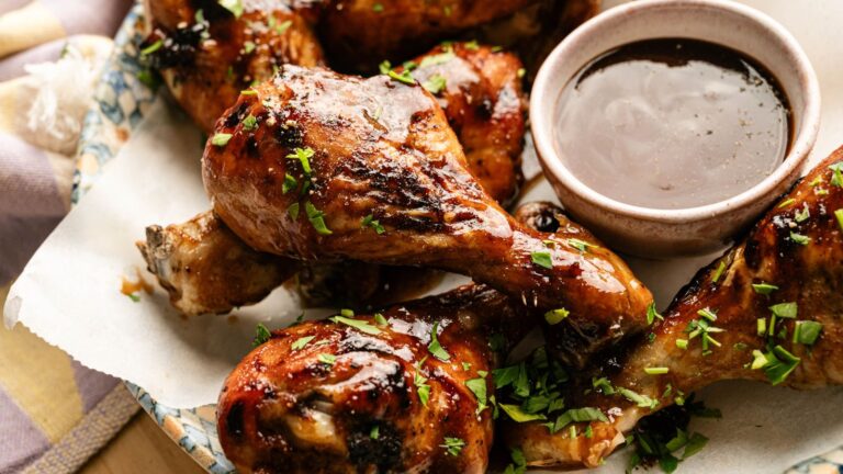 Grilled chicken drumsticks garnished with chopped herbs, served on parchment paper with a small bowl of dipping sauce.