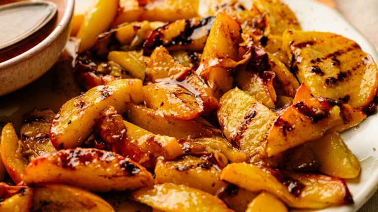 A close-up of grilled peach slices on a white plate, showing caramelized edges and a glossy coating.