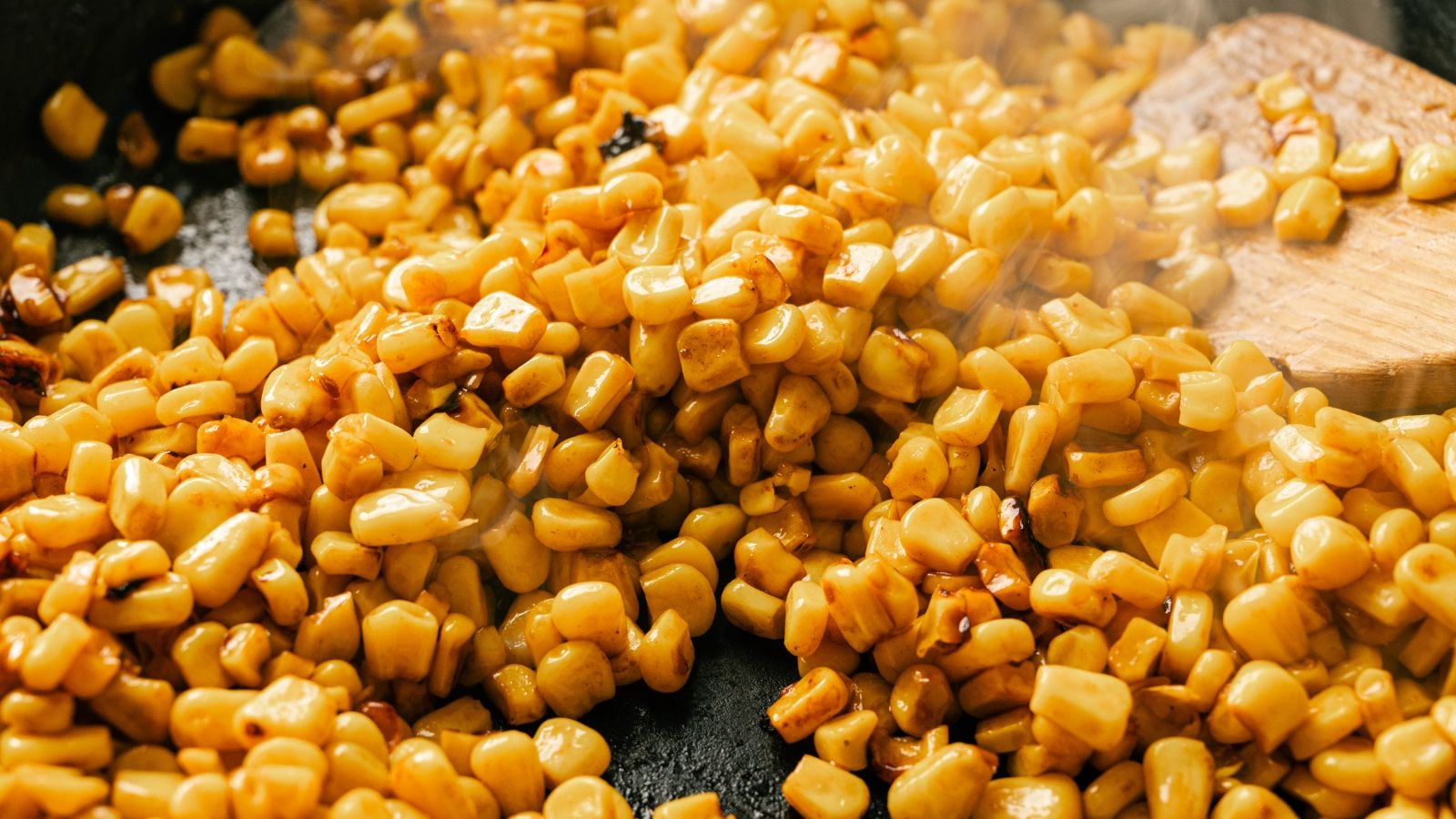 Close-up of cooked corn kernels being stirred with a wooden spatula in a pan.